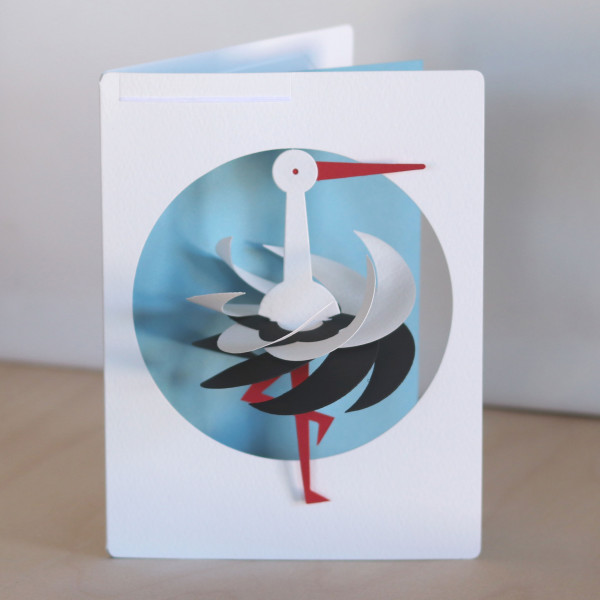 Kleiner Storch als Mobile in Postkarte vor hellblauem Hintergrund
